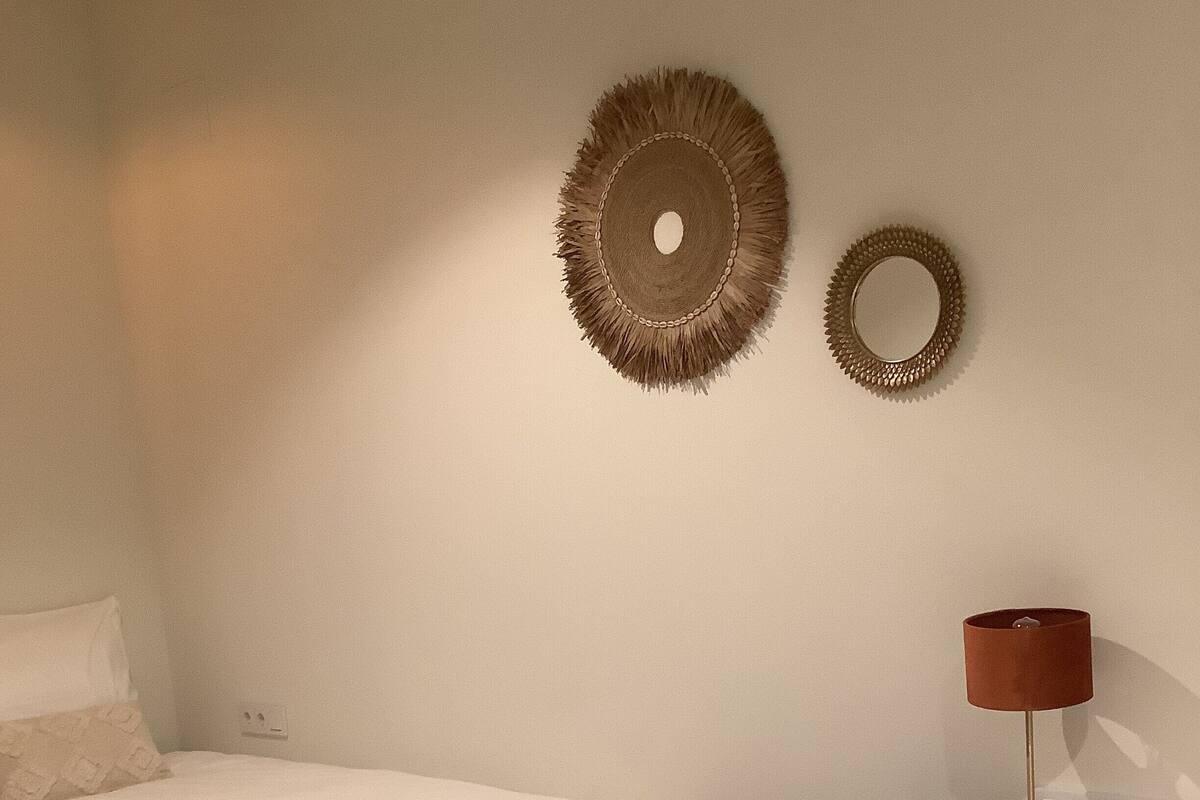Een slaapkamer met een bed, een nachtkastje met een lamp en twee decoraties aan de muur.
