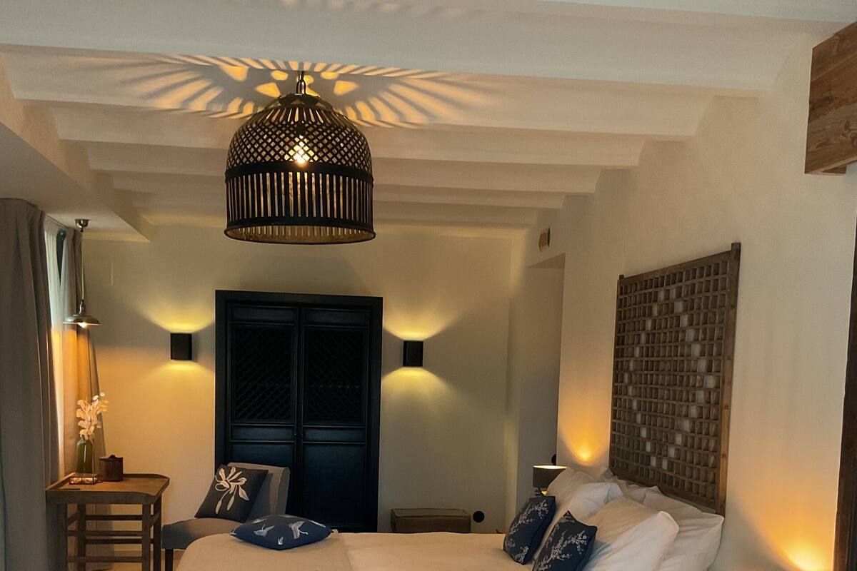 Een slaapkamer met een groot bed, nachtkastjes, een hanglamp en een deur met decoratief paneel.