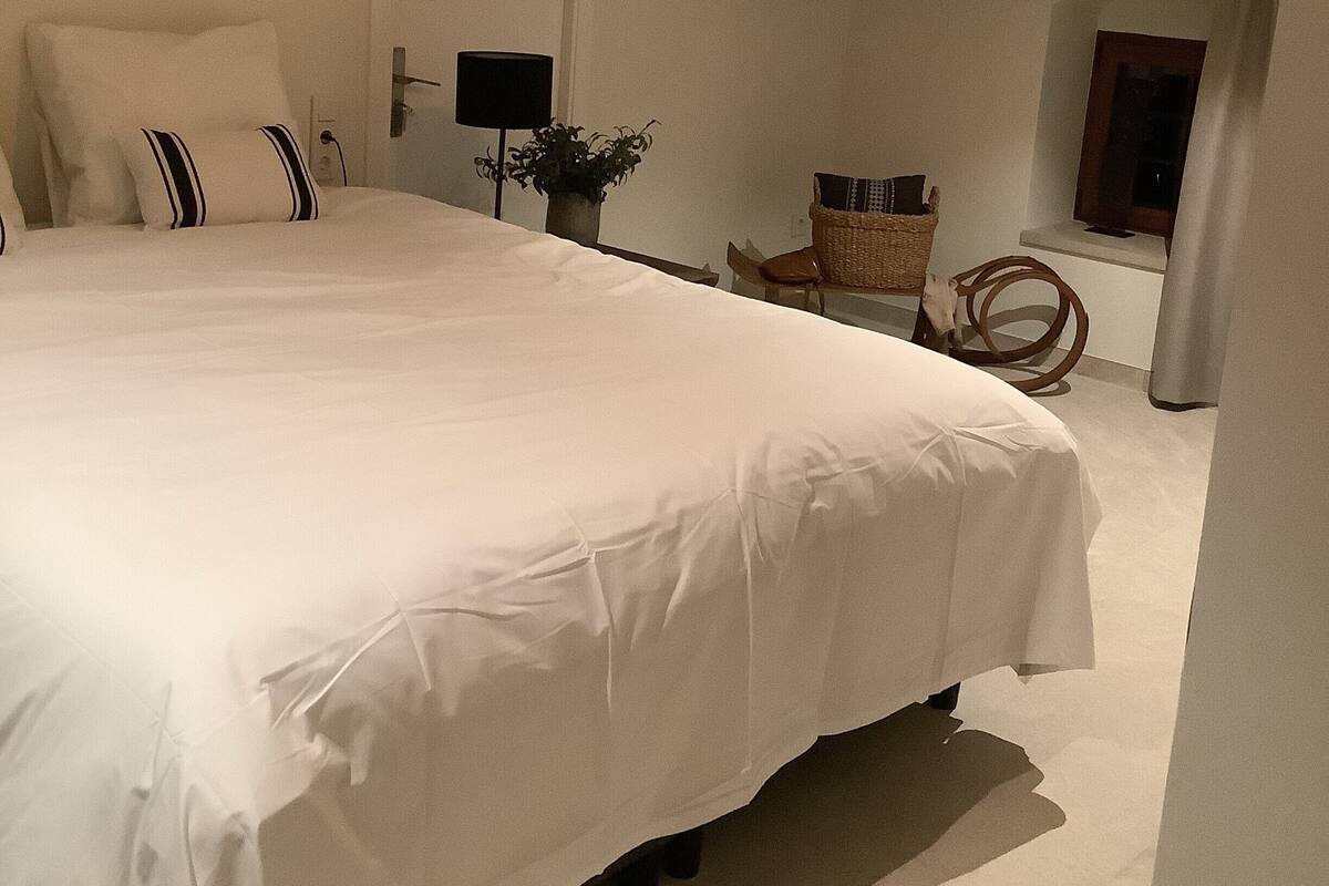 Een slaapkamer met een groot bed, een hanglamp, een houten balk, een deur, een stoel en een raam.