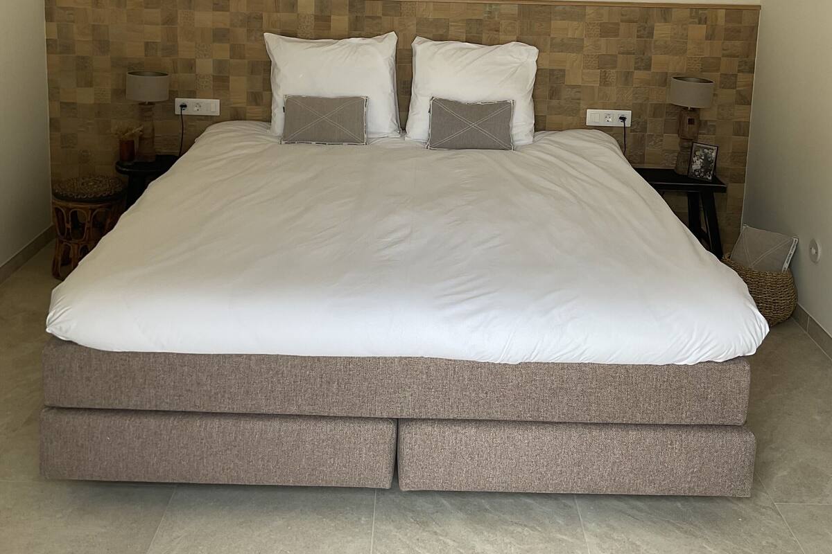 Een groot bed met houten hoofdbord, twee nachtkastjes en een hanglamp.