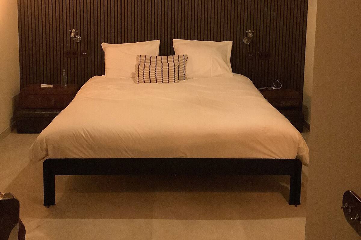 Een slaapkamer met een groot bed, een houten hoofdbord, een hanglamp en een nachtkastje met een lamp.