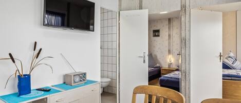 A modern room with a flat-screen TV, a small radio, a blue vase with decorative sticks, a wooden chair, and a bed with striped bedding.