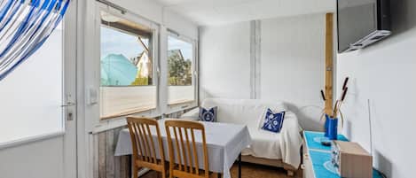 A compact room with a dining table, a sofa, and a TV mounted on the wall.