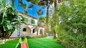 Un jardín trasero con un tobogán, una casa con arcos y abundante vegetación.
