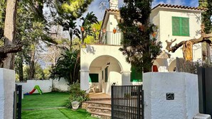 Una casa con fachada blanca, contraventanas verdes, un portón negro y un césped cuidado.