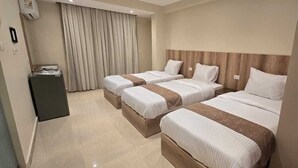 Habitación de hotel con tres camas, un escritorio y un mini bar.