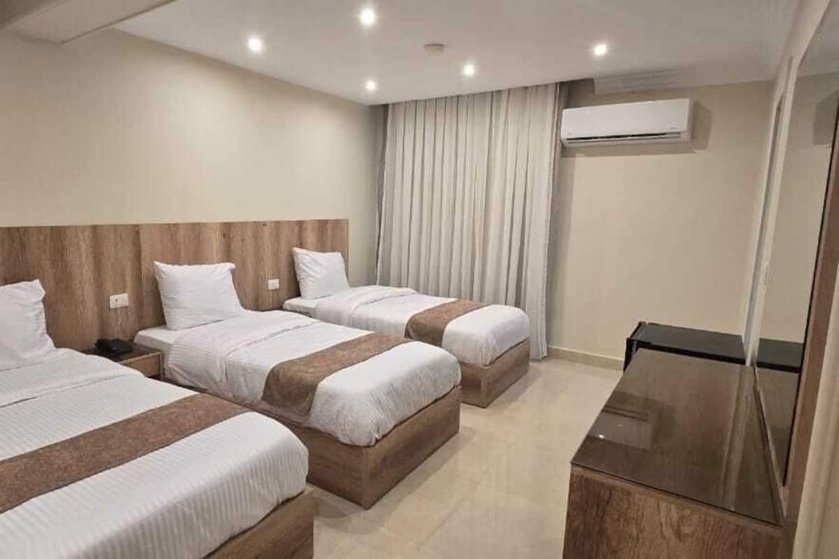 Habitación de hotel con tres camas, cabecero de madera, televisor de pantalla plana y aire acondicionado.