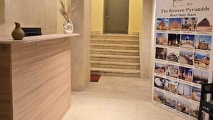 Zona de recepción de hotel con suelo de mármol, mostrador de recepción, una escalera y una pared con fotografías del recorrido por el hotel.