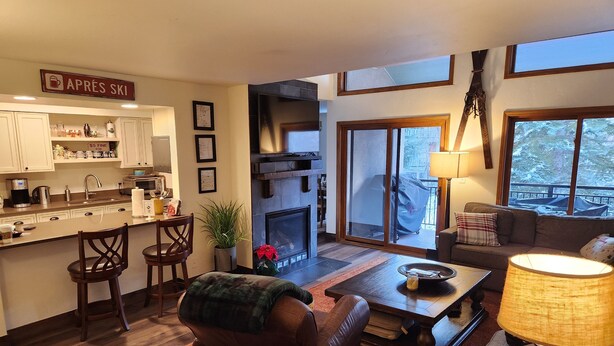 A cozy living room with a fireplace, a dining area, and a kitchen.