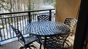 A balcony with a round table and chairs, overlooking a snowy landscape with trees and a road.