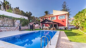 Una piscina con solárium alicatado, una casa de fachada roja y un muro de piedra.