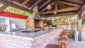 Un área de cocina al aire libre con mostrador de ladrillo, taburetes de madera y pared de piedra de fondo.