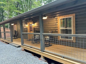 Eine rustikale Holzhütte mit Veranda, einem Willkommensschild und einer Sitzgruppe mit karierten Stühlen.