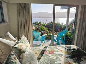 A room with a large sliding glass door leading to a balcony with a view of a body of water and hills.