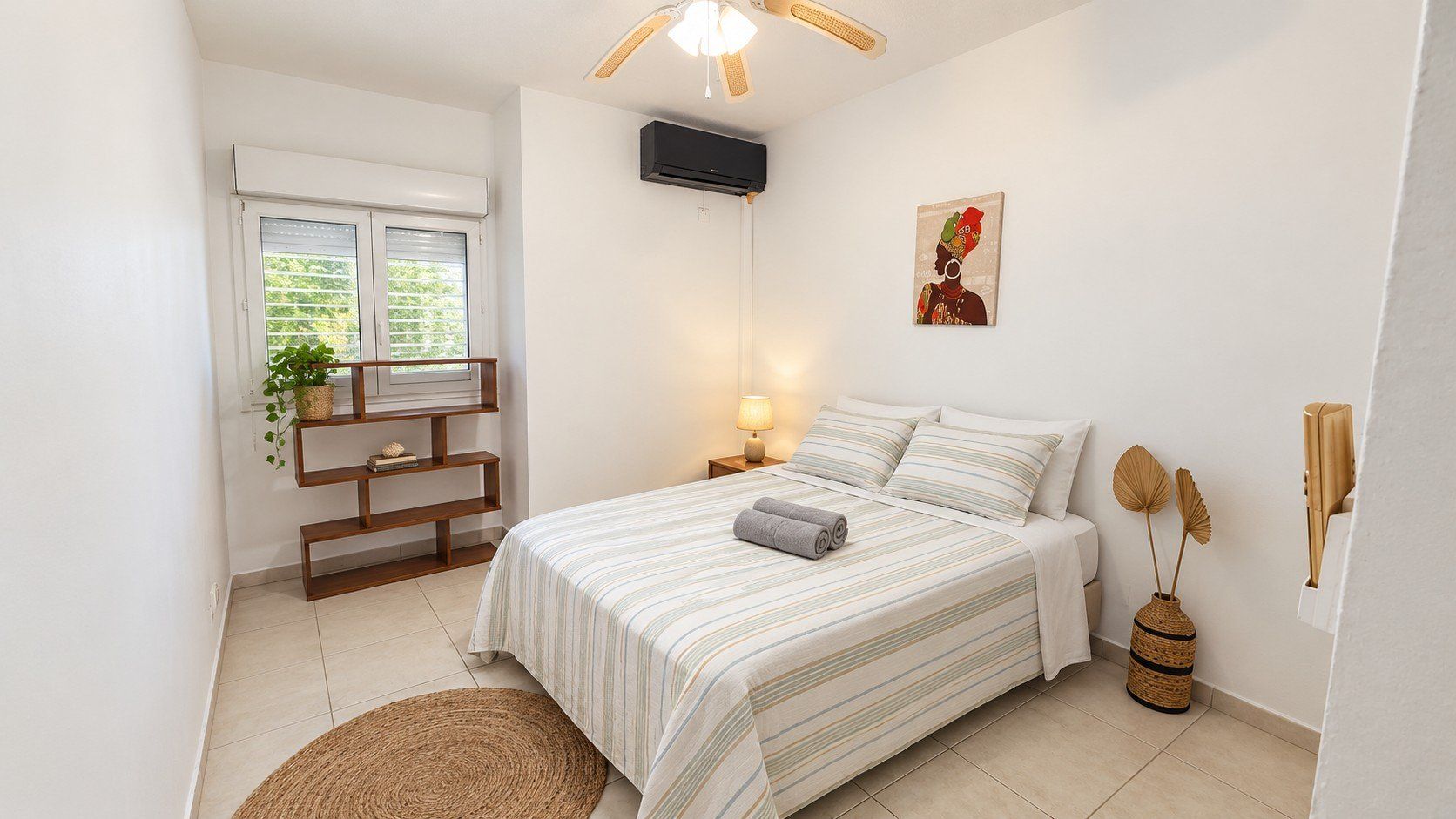 Une chambre à coucher comprenant un lit, une lampe de chevet, un climatiseur fixé au mur et une fenêtre avec des stores.