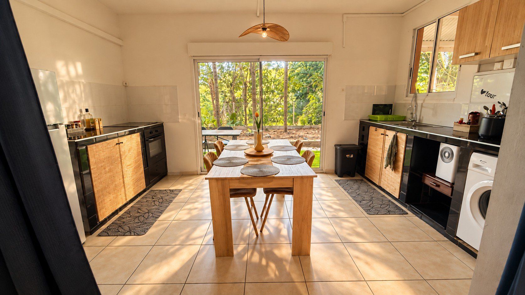 A modern kitchen with a dining area, large windows, and a view of greenery.