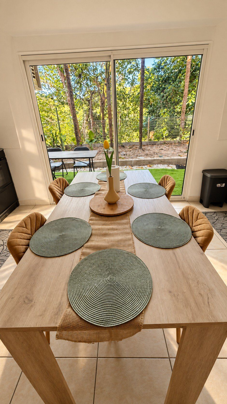 Uma sala de jantar com uma mesa comprida, quatro cadeiras e um vaso com uma única flor.