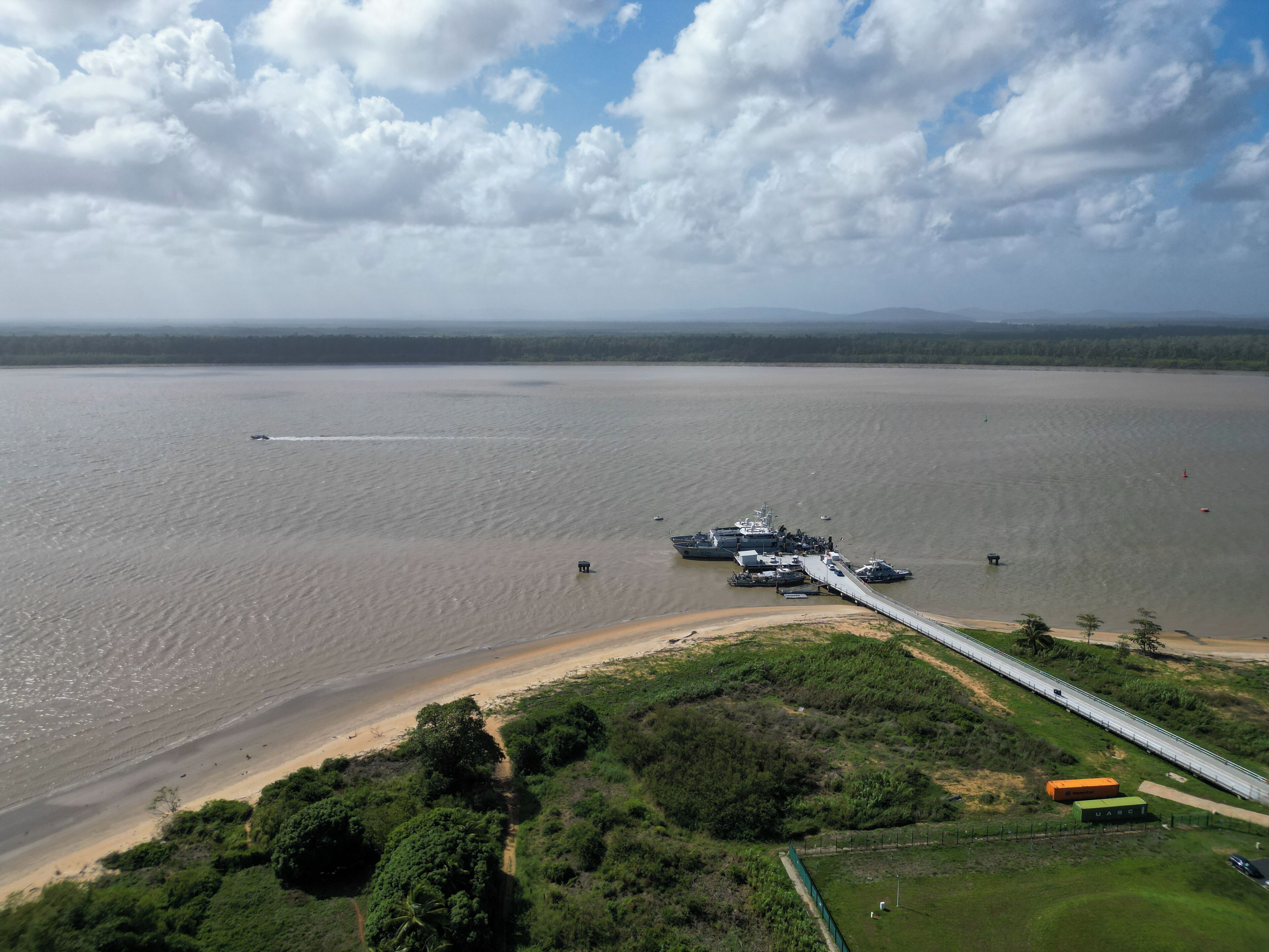 Zona costera con un puente que une dos extensiones de tierra, agua y una pequeña embarcación.