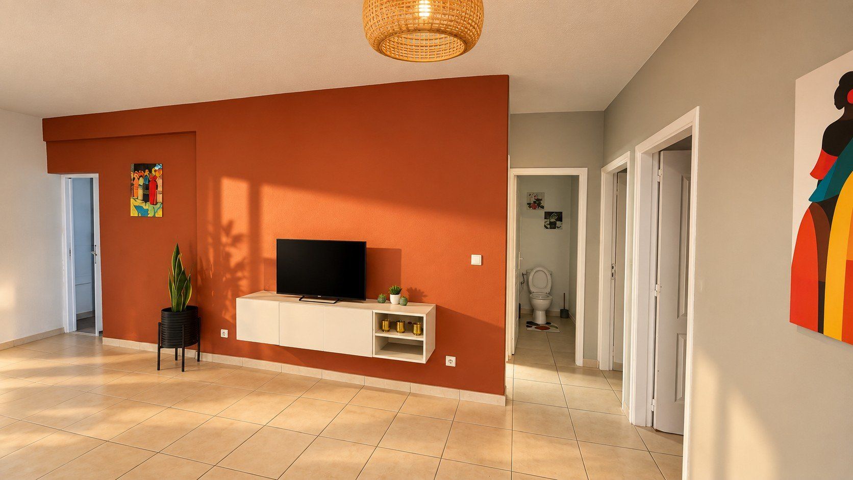 Ein modernes Wohnzimmer mit einem Flachbildfernseher auf einem weißen Schrank, einer Topfpflanze und einem farbenfrohen Kunstwerk an der Wand.