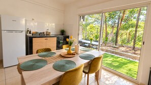 A modern kitchen with a Samsung refrigerator, a dining table with green placemats, and a view of a garden through a sliding glass door. - Hostel Toucan (Remire Montjoly)