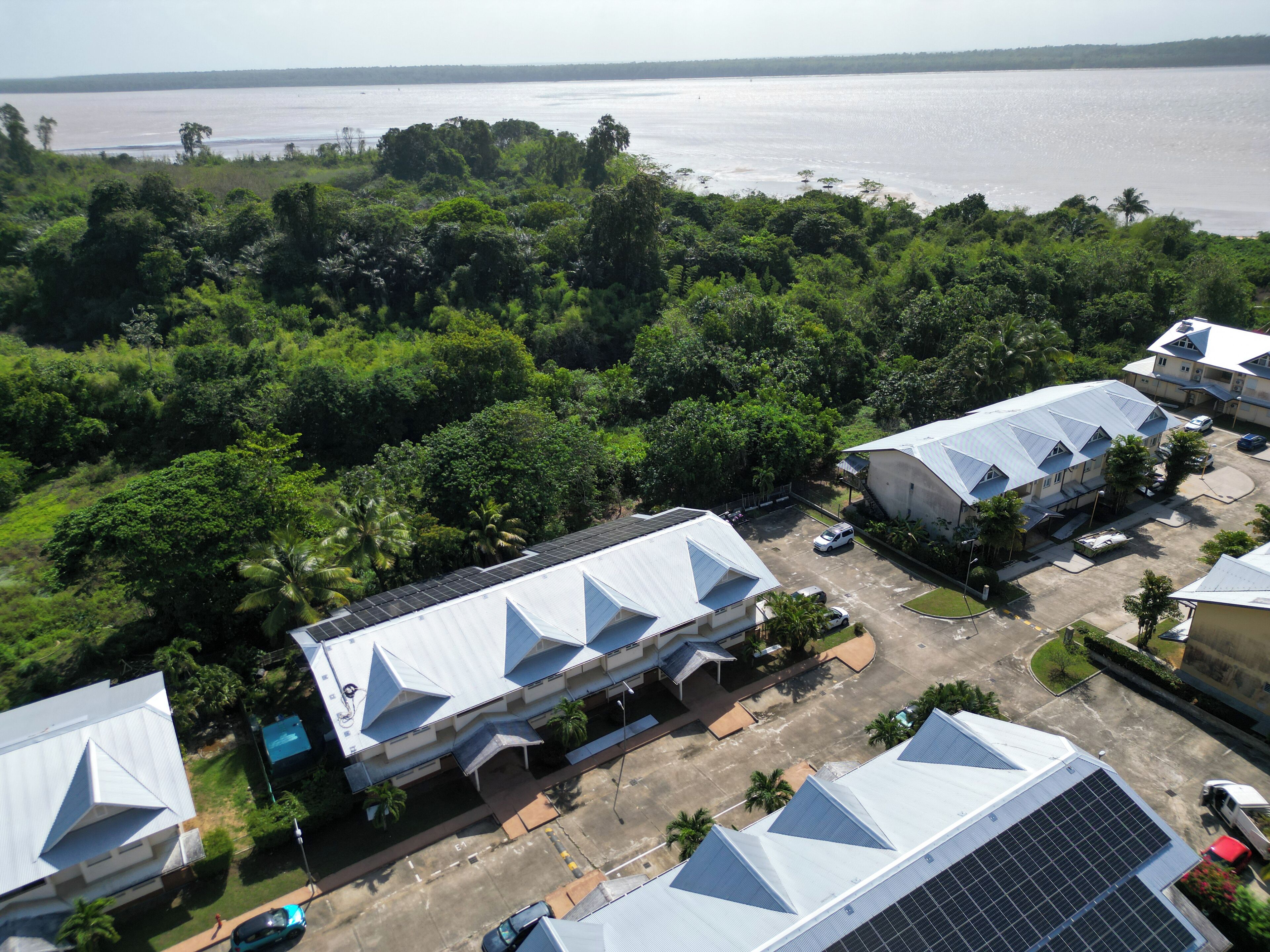 An aerial view of a resort with multiple buildings, solar panels, and a body of water in the background.