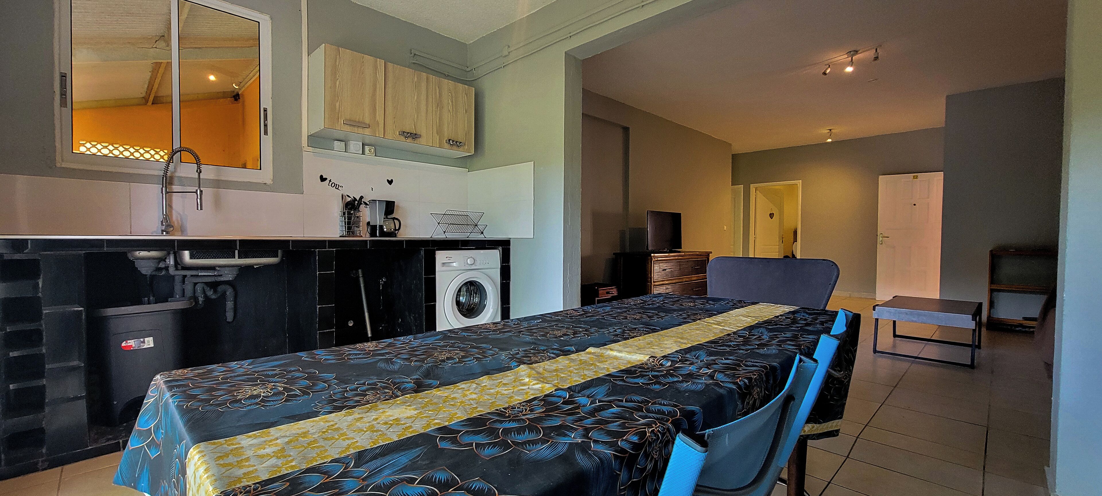 A compact room with a bed, a desk, a washing machine, and a television.