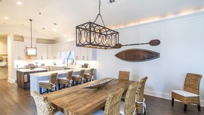 A modern kitchen with white cabinets, a wooden dining table, wicker chairs, and a unique wall-mounted paddle.