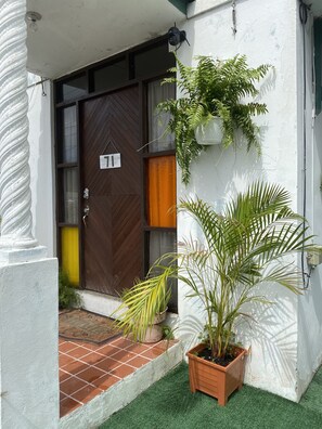 Une entrée d’immeuble avec une porte marron, une enseigne portant le numéro 11 et des plantes en pot.
