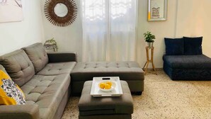 Un salon avec un canapé gris, un pouf gris, une petite table d’appoint avec une plante et un tableau encadré au mur.