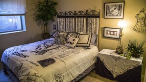 A neatly made bed with a Paris-themed bedspread, a potted plant, and a bedside table with a lamp and a framed picture. - King two bedroom apartment with full kitchen and laundry room  (St. George)