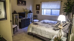 A bedroom with a bed, dresser, chair, and a window with a curtain. - King two bedroom apartment with full kitchen and laundry room  (St. George)