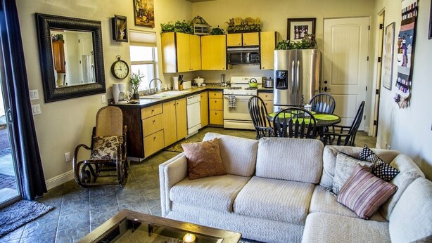 A cozy living room with a sofa and a coffee table, a kitchen with yellow cabinets and modern appliances, and a dining area with a table and chairs. - King two bedroom apartment with full kitchen and laundry room  (St. George)