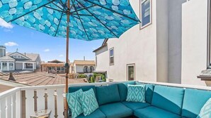 A balcony with a blue patterned umbrella, a teal sofa with patterned cushions, and a small table.