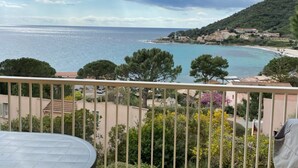 En balkon med udsigt over en kystby, inklusive en strand og et kuperet landskab.