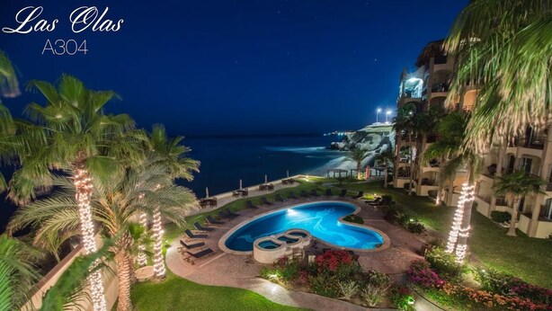 Ein Nachtblick auf einen Hotel-Poolbereich mit einem gewundenen Pool, Palmen und Blick auf den Ozean.