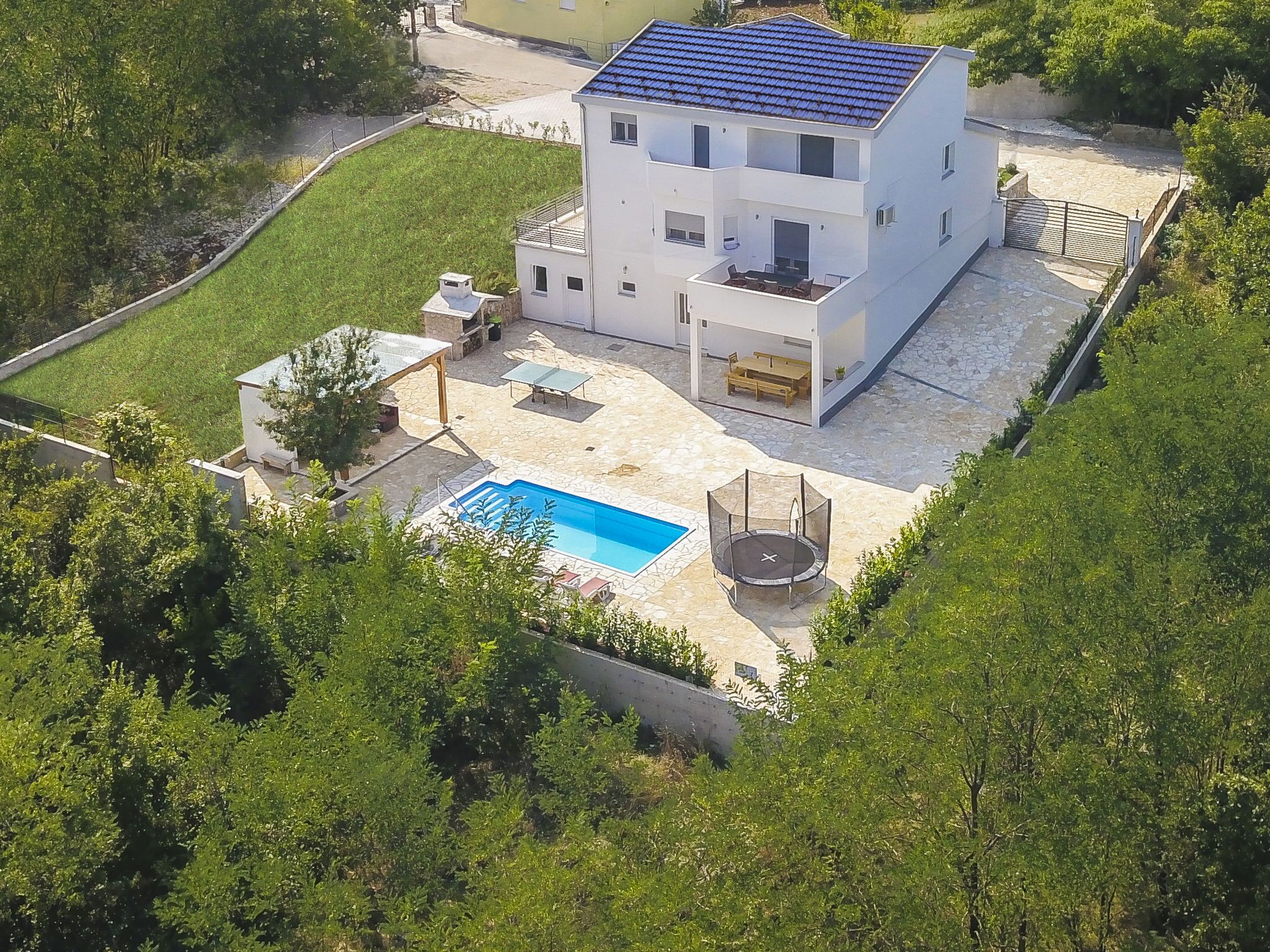 A modern two-story house with a swimming pool, outdoor seating, and a trampoline.