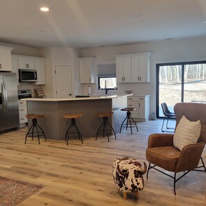 A modern kitchen with white cabinets, a central island with stools, a refrigerator, and a microwave. - Luxurious Silver Lake/Dunes Brand New Home (Mears)