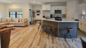 Une cuisine moderne dotée d’un îlot central, d’un revêtement de sol en bois et d’un coin salon avec un canapé et des tabourets.