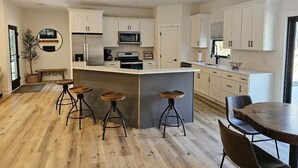Une cuisine moderne avec des meubles blancs, un îlot central doté de tabourets et un coin repas comprenant une table ronde et des chaises.