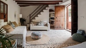 Una sala de estar acogedora con un sofá blanco, un otoman redondos y una escalera que sube a un nivel superior.