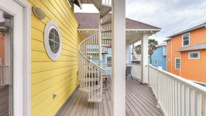 A wooden deck with a white railing, a yellow building with a window, and a blue building in the background.