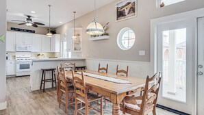 A spacious kitchen with white cabinets, a wooden dining table, and a ceiling fan.
