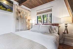 Relax in a spacious bedroom with a large bed, featuring crisp white linens, and enjoy a view of the outdoors from the window.