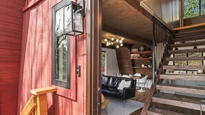 Un escalier en bois mène à un espace de vie comprenant un canapé en cuir noir, une table à manger et une rambarde en bois.