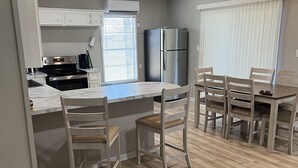 Una cocina moderna con armarios blancos, un refrigerador de acero inoxidable y un horno empotrado. Cuenta con una zona de comedor con sillas de madera y una mesa.