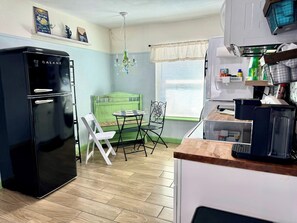 Une cuisine de taille réduite avec un réfrigérateur noir, une table à manger avec des chaises, un banc vert et une fenêtre avec des stores.