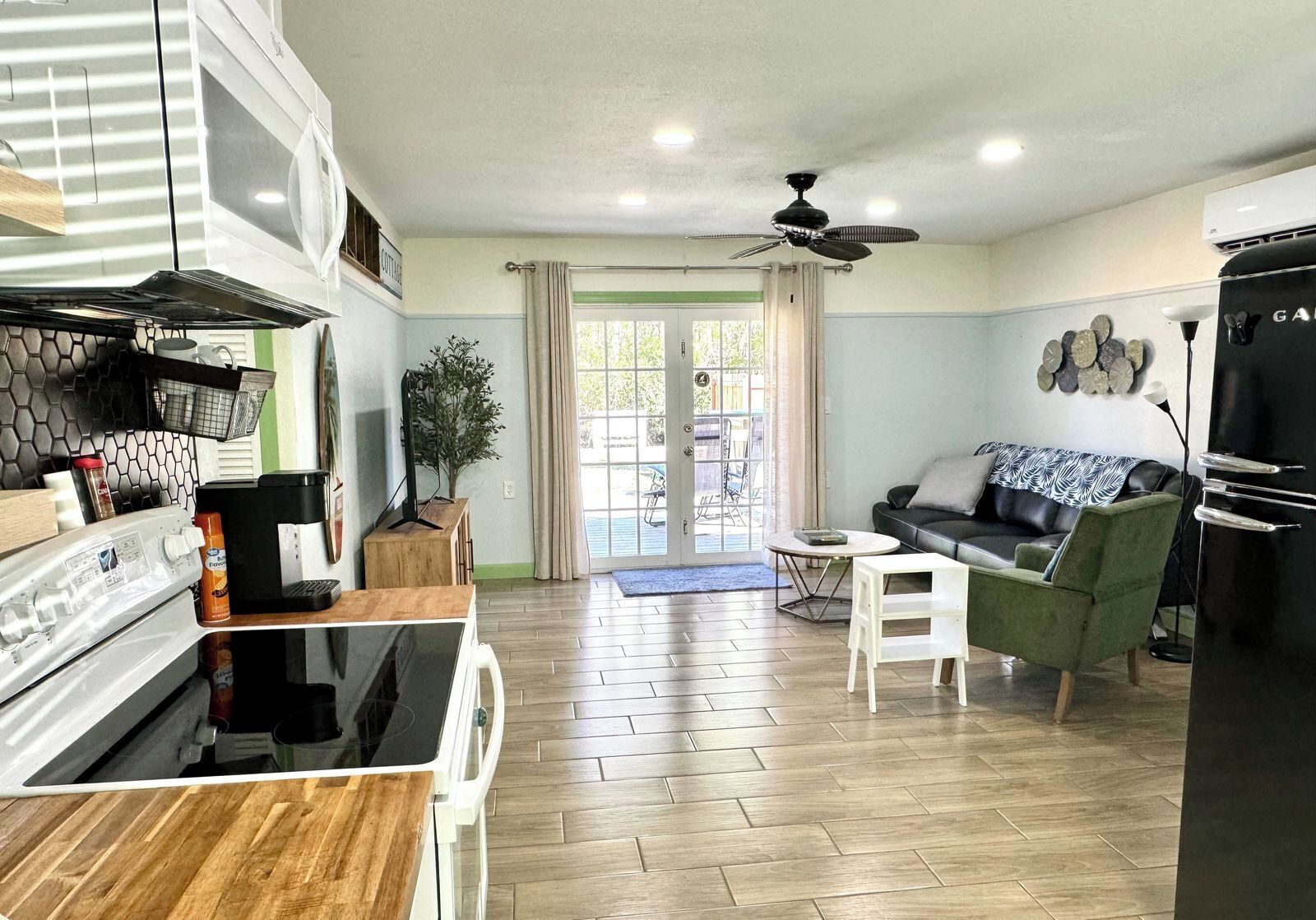 A modern kitchen with a stove, refrigerator, and dining area. There is a dining table and a sofa in the living room.