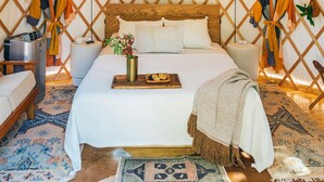 A cozy, well-lit tent with a wooden bed, a tray with cookies, and a vase with flowers. - The Macaw Yurt at Camposanto ATX Glamping on Lake Travis (Lakeway)