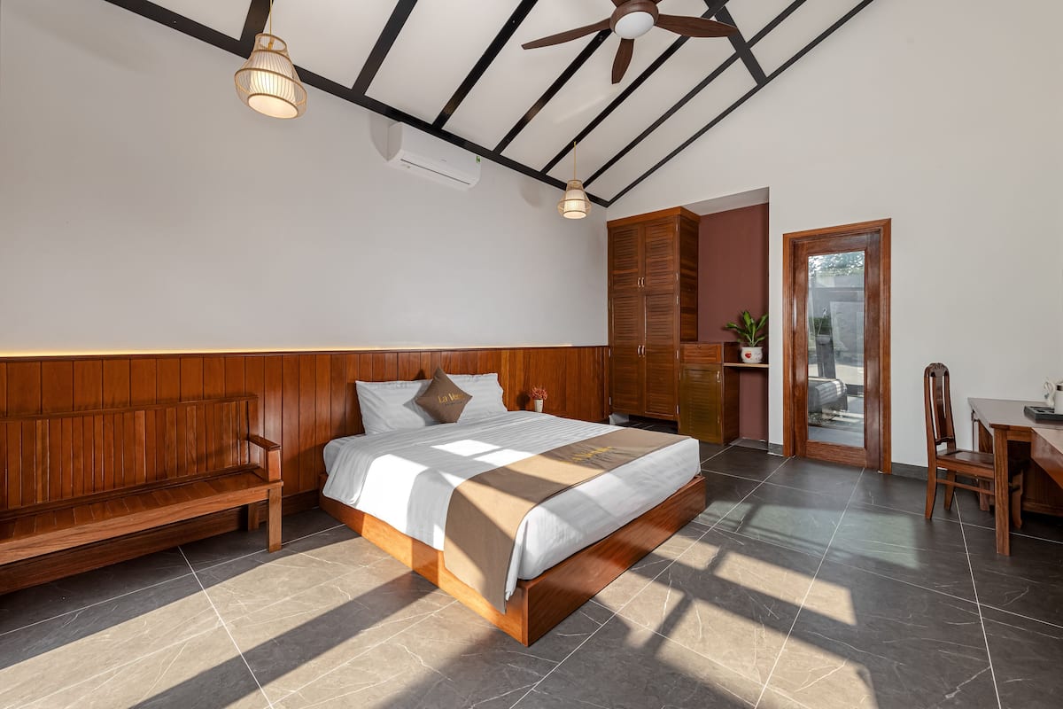 A bedroom with a wooden bed, a bench, a desk, and a ceiling fan.