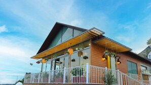 A modern house with a wooden facade, large windows, and a balcony with white railings.